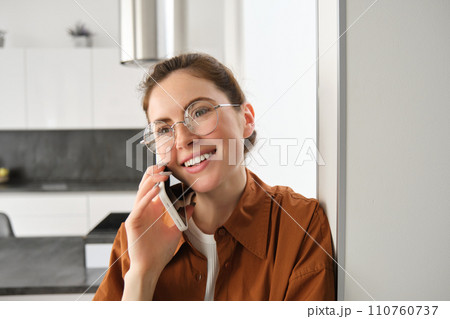 Portrait of happy smiling young woman at home, talking on mobile phone, calling friend and having nice conversation, answer telephone 110760737