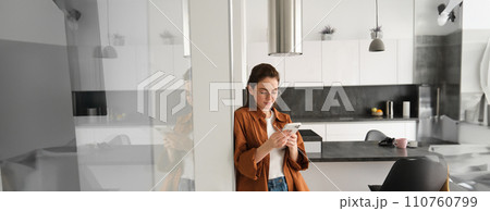 Portrait of cute young woman standing at home with smartphone, reading message on mobile phone, using application, order online, paying utility bill in app 110760799