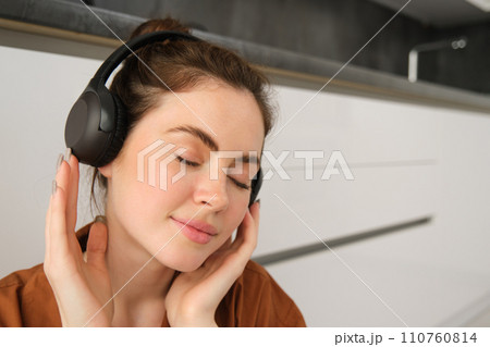 Portrait of attractive young woman in wireless headphones, smiling with closed eyes, relaxing with favourite songs on playlist Portrait of attractive young woman in wireless headphones, smiling with closed eyes, relaxing with favourite songs on playlist 110760814