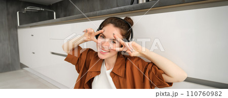 Happy young woman in headphones, listens music, enjoys sound quality, shows v-sign Happy young woman in headphones, listens music, enjoys sound quality, shows v-sign 110760982