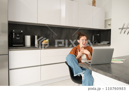 Work from home, remote job concept. Young woman sitting in kitchen, using laptop, joins video chat conversation, give online lessons, talking to client on computer Work from home, remote job concept. Young woman sitting in kitchen, using laptop, joins video chat conversation, give online lessons, talking to client on computer 110760983