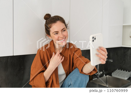 Lifestyle shot of young woman video chatting, using smartphone app to talk online, records herself for social media blog, looks happy 110760999