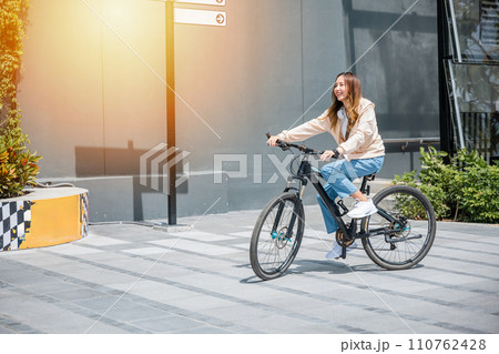Happy Asian young woman riding bicycle on street outdoor near building city, Portrait of smiling female lifestyle use mountain bike in summer travel means of transportation, ECO friendly, Urban biking Happy Asian young woman riding bicycle on street outdoor near building city, Portrait of smiling female lifestyle use mountain bike in summer travel means of transportation, ECO friendly, Urban biking 110762428