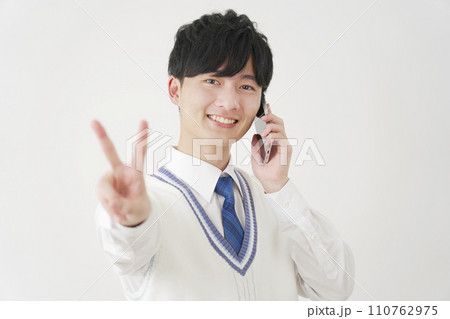 スマートフォンで電話しながらピースサインをする男子高校生　白背景 110762975