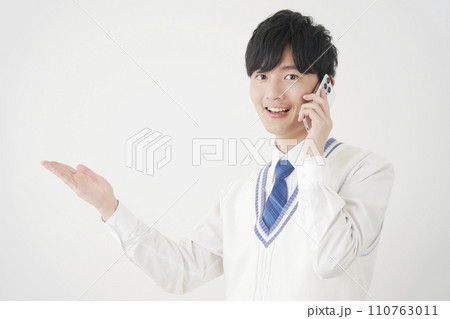 スマートフォンで電話しながら手のひらで左側を指す男子高校生 白背景 スマートフォンで電話しながら手のひらで左側を指す男子高校生 白背景 110763011