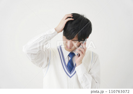 頭を抱えながらスマートフォンで電話する男子高校生 白背景 頭を抱えながらスマートフォンで電話する男子高校生 白背景 110763072
