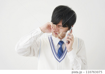 泣きながらスマートフォンで電話する男子高校生　白背景 110763075