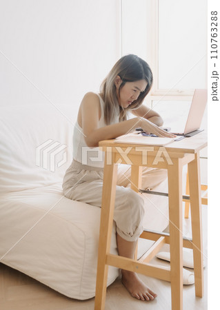 Serious freelance woman is working online at home with computer laptop and taking notes in her apartment. 110763288