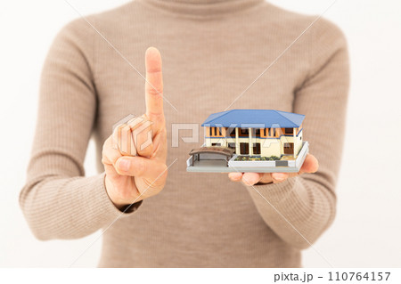 戸建ての住宅模型を持って人差し指を立てるミドル女性 110764157