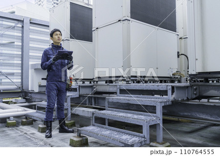 デニムの作業着を着てビルの屋上で点検作業をする若い男性のポートレート　撮影協力:有明教育芸術短期大学 110764555
