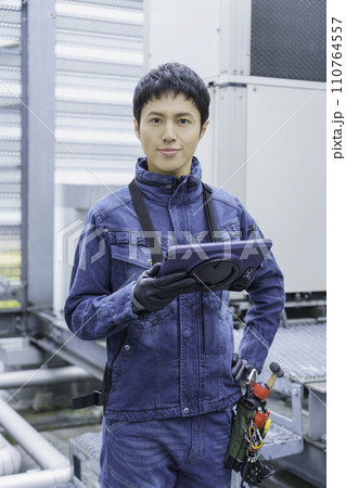 デニムの作業着を着てビルの屋上で点検作業をする若い男性のポートレート　撮影協力:有明教育芸術短期大学 110764557