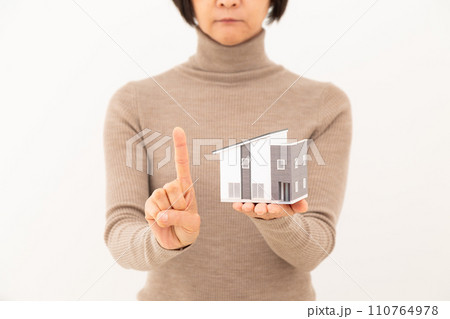 戸建ての住宅模型を持って人差し指を立てるミドル女性 戸建ての住宅模型を持って人差し指を立てるミドル女性 110764978