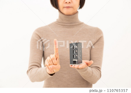 ビルの住宅模型を持って人差し指を立てるミドル女性 ビルの住宅模型を持って人差し指を立てるミドル女性 110765357