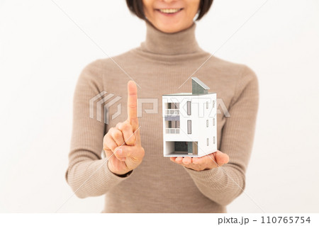 戸建ての住宅模型を持って人差し指を立てるミドル女性 110765754