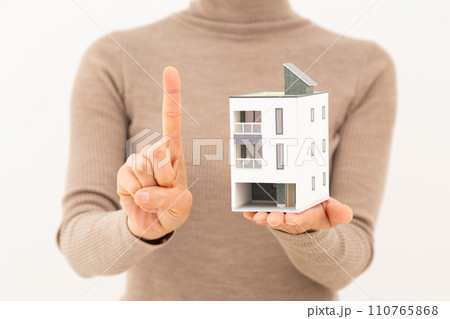 戸建ての住宅模型を持って人差し指を立てるミドル女性 110765868