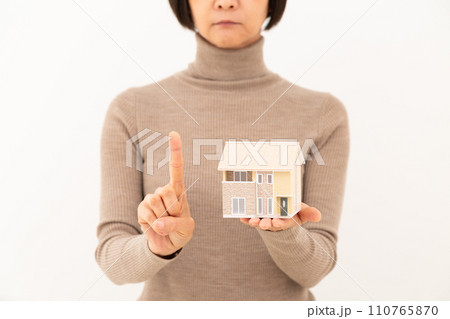戸建ての住宅模型を持って人差し指を立てるミドル女性 110765870