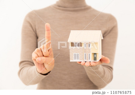 戸建ての住宅模型を持って人差し指を立てるミドル女性 110765875