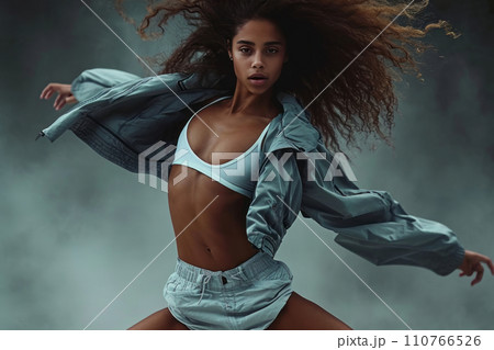 AI-generated content. Studio portrait of a beautiful Hispanic young woman in a dynamic dance pose. Sexy Latin model wearing casual street clothes against grey background, dramatic lighting. 110766526