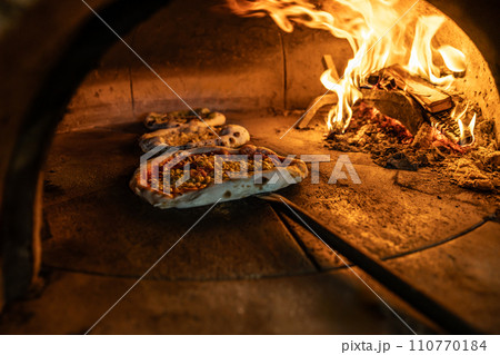 Traditional oven for baking pizza with burning wood and shovel. The cook rotates the pizza in the oven to ensure even baking Traditional oven for baking pizza with burning wood and shovel. The cook rotates the pizza in the oven to ensure even baking 110770184