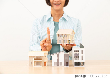 戸建ての住宅模型を持って人差し指を立てるミドル女性 110770582