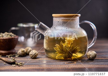 Teapot and glass cup with blooming tea flower inside on a wooden table 110771837
