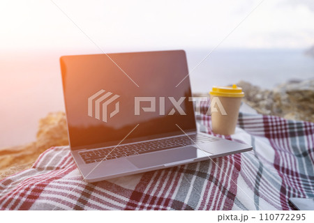 Laptop coffee on blanket with ocean view. Illustrating serene outdoor laptop use. Freelancer enjoying their time outdoors while working or browsing the internet. Laptop coffee on blanket with ocean view. Illustrating serene outdoor laptop use. Freelancer enjoying their time outdoors while working or browsing the internet. 110772295