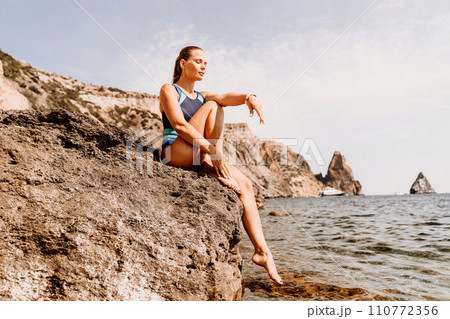 Woman beach vacation photo. A happy tourist in a blue bikini enjoying the scenic view of the sea and volcanic mountains while taking pictures to capture the memories of her travel adventure. 110772356