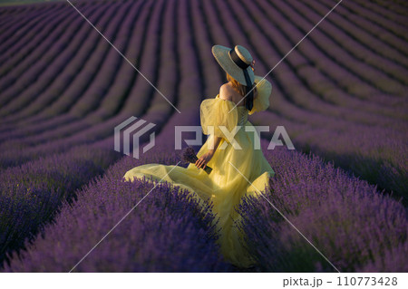Back view woman lavender sunset. Happy woman in yellow dress holds lavender bouquet. Aromatherapy concept, lavender oil, photo session in lavender Back view woman lavender sunset. Happy woman in yellow dress holds lavender bouquet. Aromatherapy concept, lavender oil, photo session in lavender 110773428