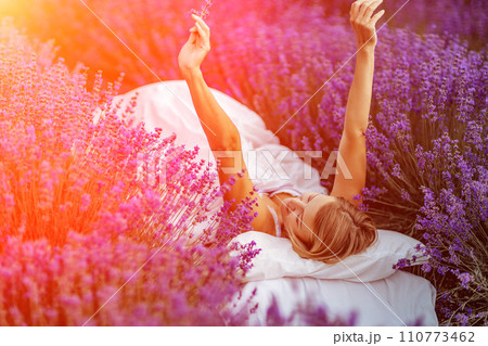 Woman lavender field. A middle-aged woman lies in a lavender field and enjoys aromatherapy. Aromatherapy concept, lavender oil, photo session in lavender 110773462