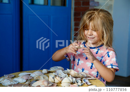 Little preschool girl with variation of different shells and clams at home. Happy child with collected shell from Normandy, France. Children, education, vacation concept. Little preschool girl with variation of different shells and clams at home. Happy child with collected shell from Normandy, France. Children, education, vacation concept. 110777856