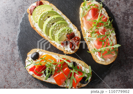 Set of open toasted bruschetta with arugula, jamon, vegetables, cream cheese close-up on a slate board. Horizontal top view 110779902