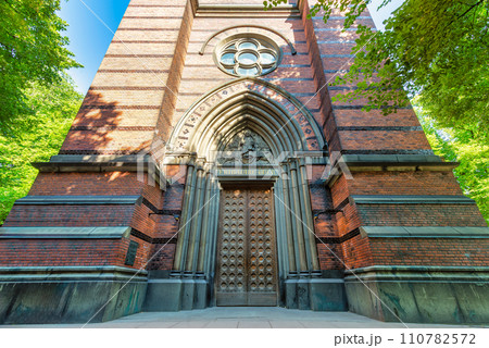 Sun shines through leaves, casting warm glow on St. Clara's Church door in Stockholm, Sweden 110782572
