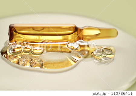 Ampoule in a drop of cosmetic gel on a green background. Ampoule in a drop of cosmetic gel on a green background. 110786411