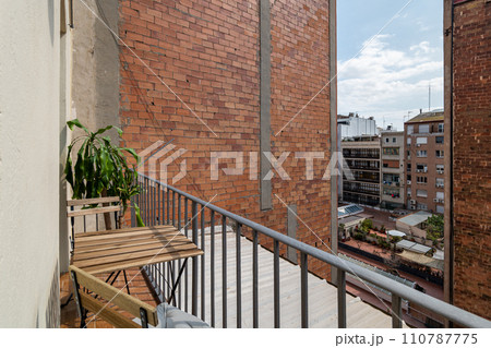 View from the terrace to the courtyard of a multi-storey new building complex on a sunny summer day. Table and chair on an open balcony in a new building 110787775