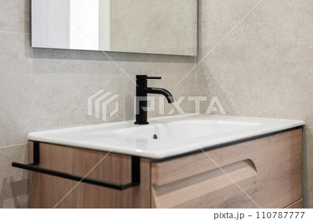 Close-up of a sink with a black tap and a mirror on the background of a gray stone wall. Concept new and stylish plumbing in new residential complexes ready for delivery 110787777