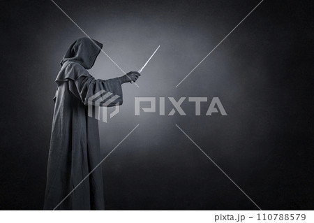 Wizard with hooded cape and magic wand over dark misty background Wizard with hooded cape and magic wand over dark misty background 110788579