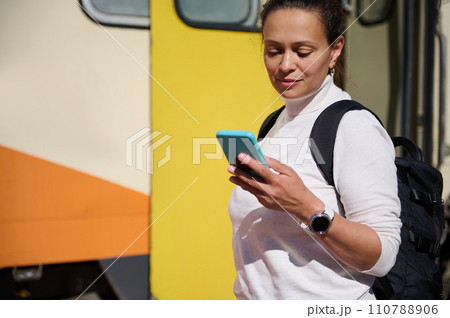 Caucasian pretty woman, tourist traveler checking mobile app on smartphone, standing against colorful train background 110788906