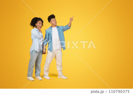 A joyful young woman and man hold hands, with the man pointing and looking away in excitement 110790375