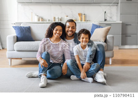 Smiling black family with son sitting on floor in cozy living room Smiling black family with son sitting on floor in cozy living room 110790411