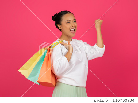 Big Discounts. Happy young asian woman carrying shopping bags and shaking fist Big Discounts. Happy young asian woman carrying shopping bags and shaking fist 110790534