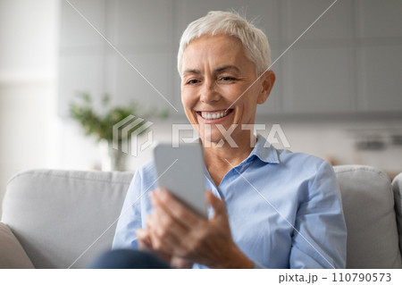 Portrait of happy mature lady surfing internet communicating on cellphone 110790573