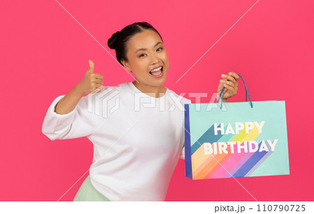 Asian woman showing thumb up, holding shopping bag with 'Happy Birthday' text 110790725