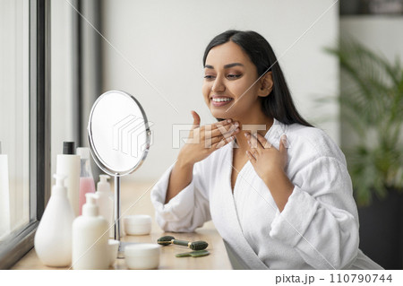 Positive millennial indian woman checking her neck in the mirror 110790744