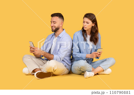 Man and woman sitting back-to-back, focused on their smartphones Man and woman sitting back-to-back, focused on their smartphones 110790881