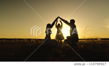 Silhouettes of parents intertwine above daughter head in meadow at sunset twilight 110790927