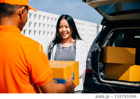 A smiling woman customer receives a cardboard parcel from a delivery service courier man at her home door showcasing efficient and modern home delivery logistics. A smiling woman customer receives a cardboard parcel from a delivery service courier man at her home door showcasing efficient and modern home delivery logistics. 110791066