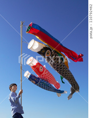 青空のもと鯉のぼりを掲げる少年 110792462
