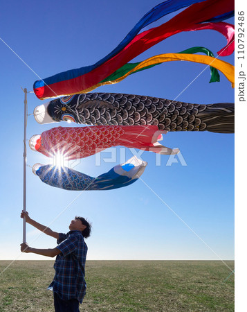 青空のもと鯉のぼりを掲げる少年 110792486