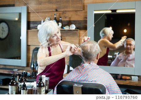 Mature woman master completes creation of senior male clients image with help of scissors 110793760