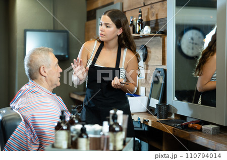 Young hairdresser girl is discussing haircut with elderly male client in barbershop Young hairdresser girl is discussing haircut with elderly male client in barbershop 110794014